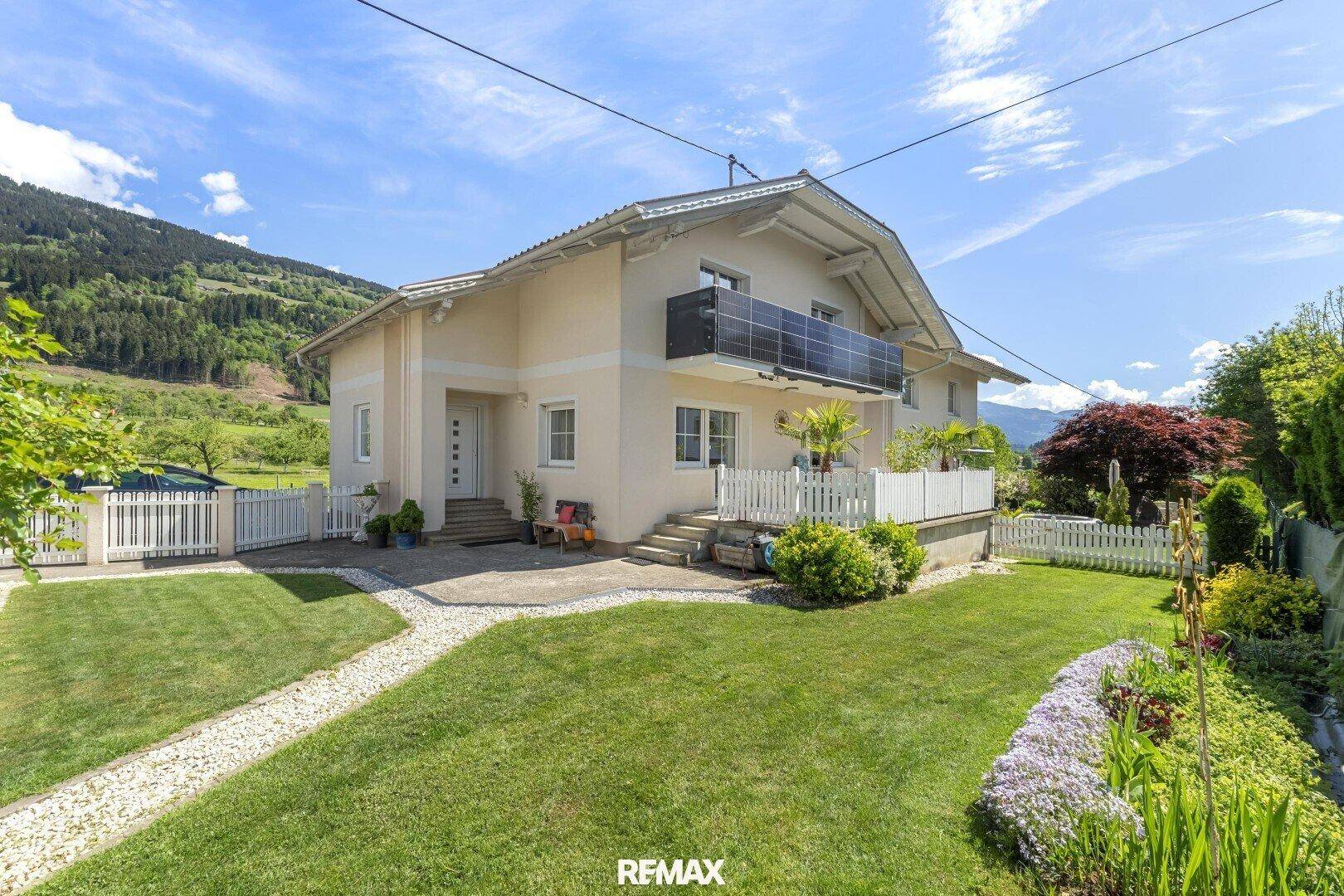 Vorderansicht des Hauses mit gepflegtem Rasen, Blumenbeeten und einem Balkon mit Solarpaneelen.