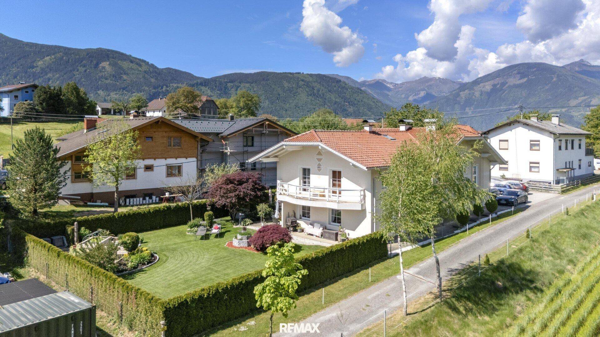 Das Haus mit Balkon und gepflegtem Garten, umgeben von einer Hecke und mit Bergblick.
