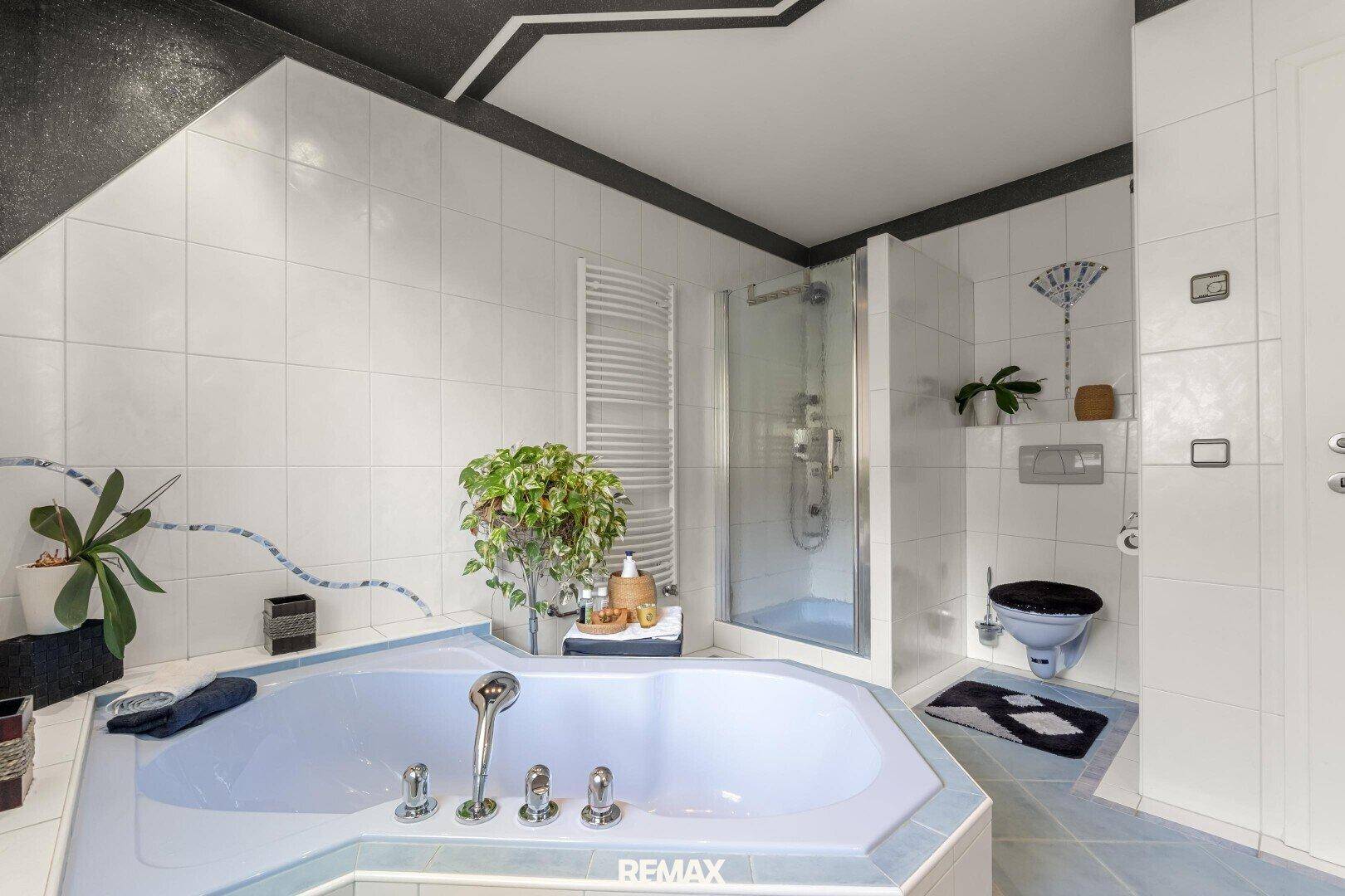 Helles Badezimmer mit großer Eckbadewanne, separater Dusche und weiß-blauen Fliesen.
