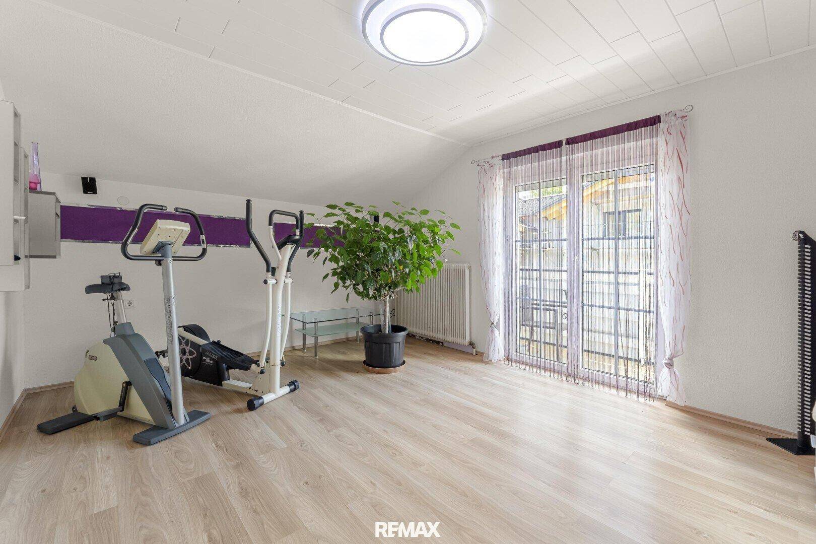 Heller Raum mit Fitnessgeräten, Pflanzen und Zugang zu einem Balkon oder einer Terrasse.