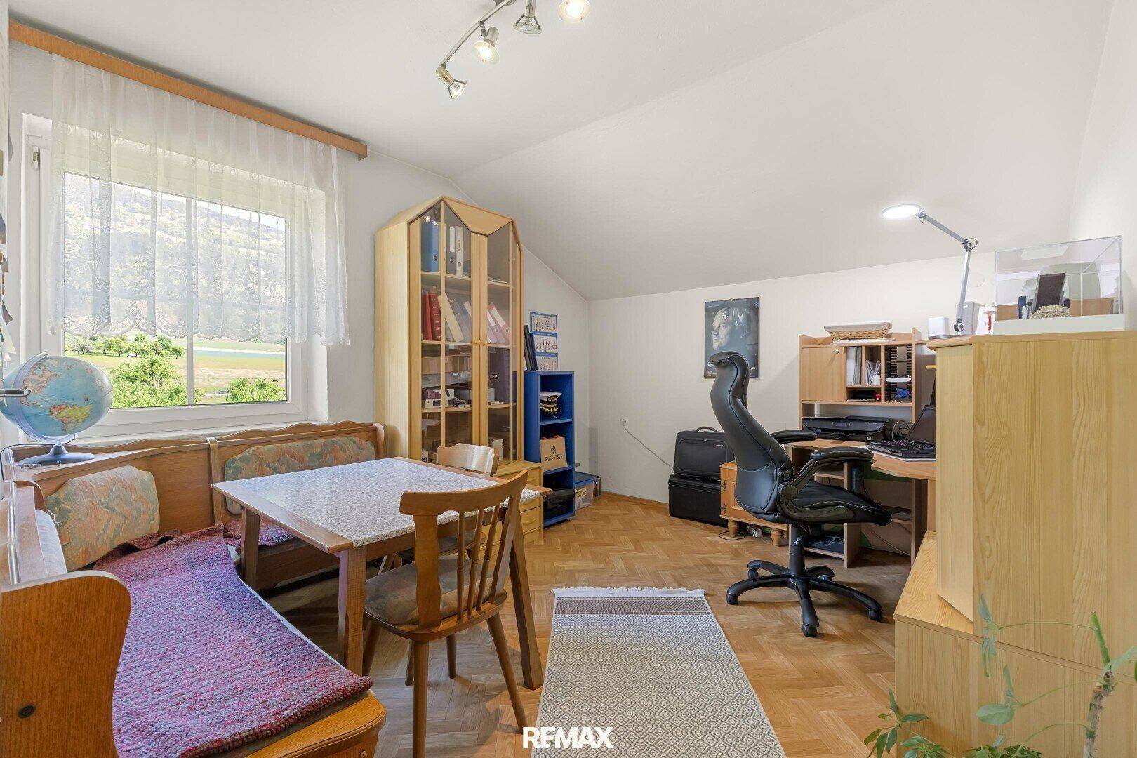 Vielseitiger Raum mit Schreibtisch, Essbereich und Fenster unter einer Dachschräge.