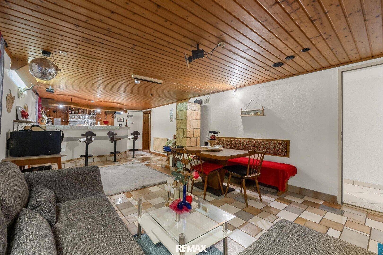 Gemütlicher Keller-Wohnbereich mit Bar, Essplatz, Sofa und traditionellem Kachelofen.