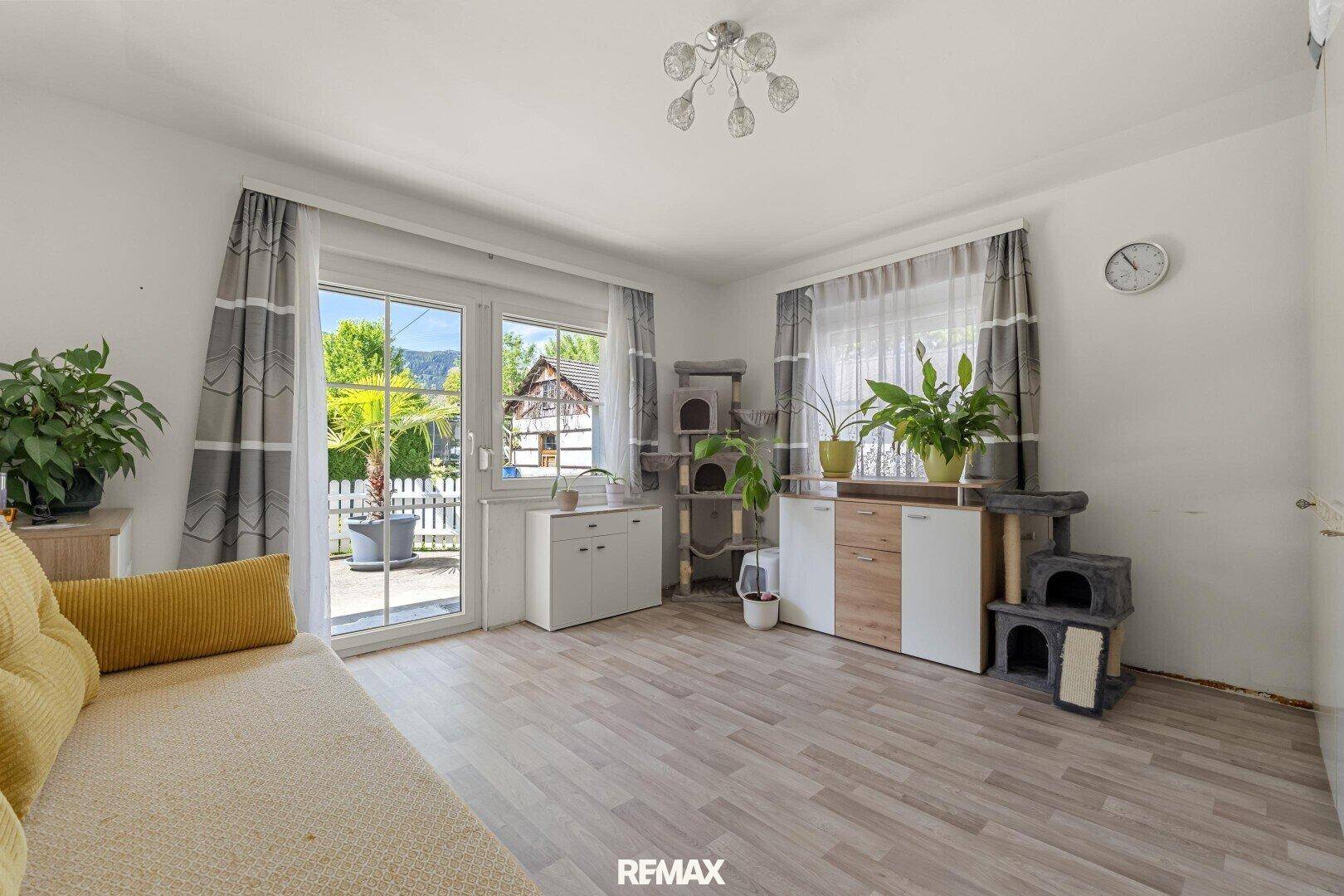 Helles Wohnzimmer mit Sofa, Katzenmöbeln und großem Fenster mit Zugang zum Garten.