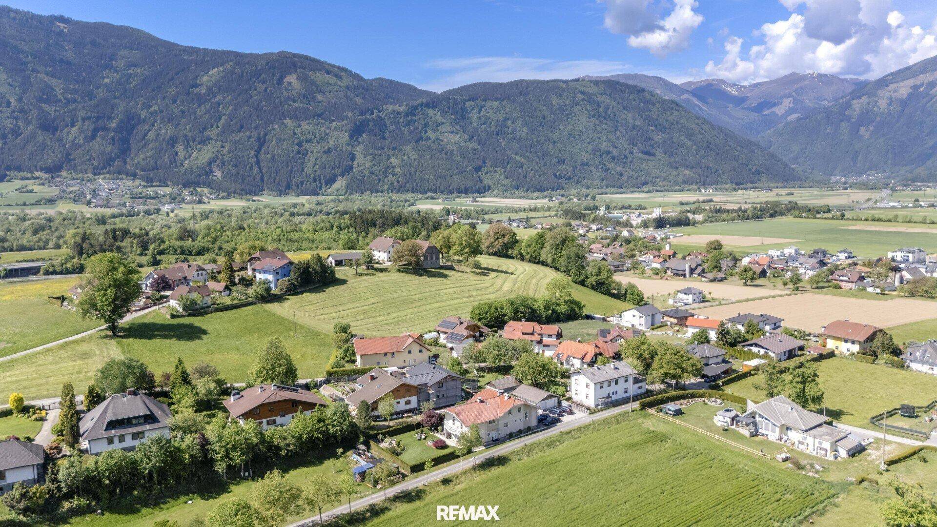 Malerische Luftaufnahme eines Dorfes eingebettet in grüne Felder und Berge.