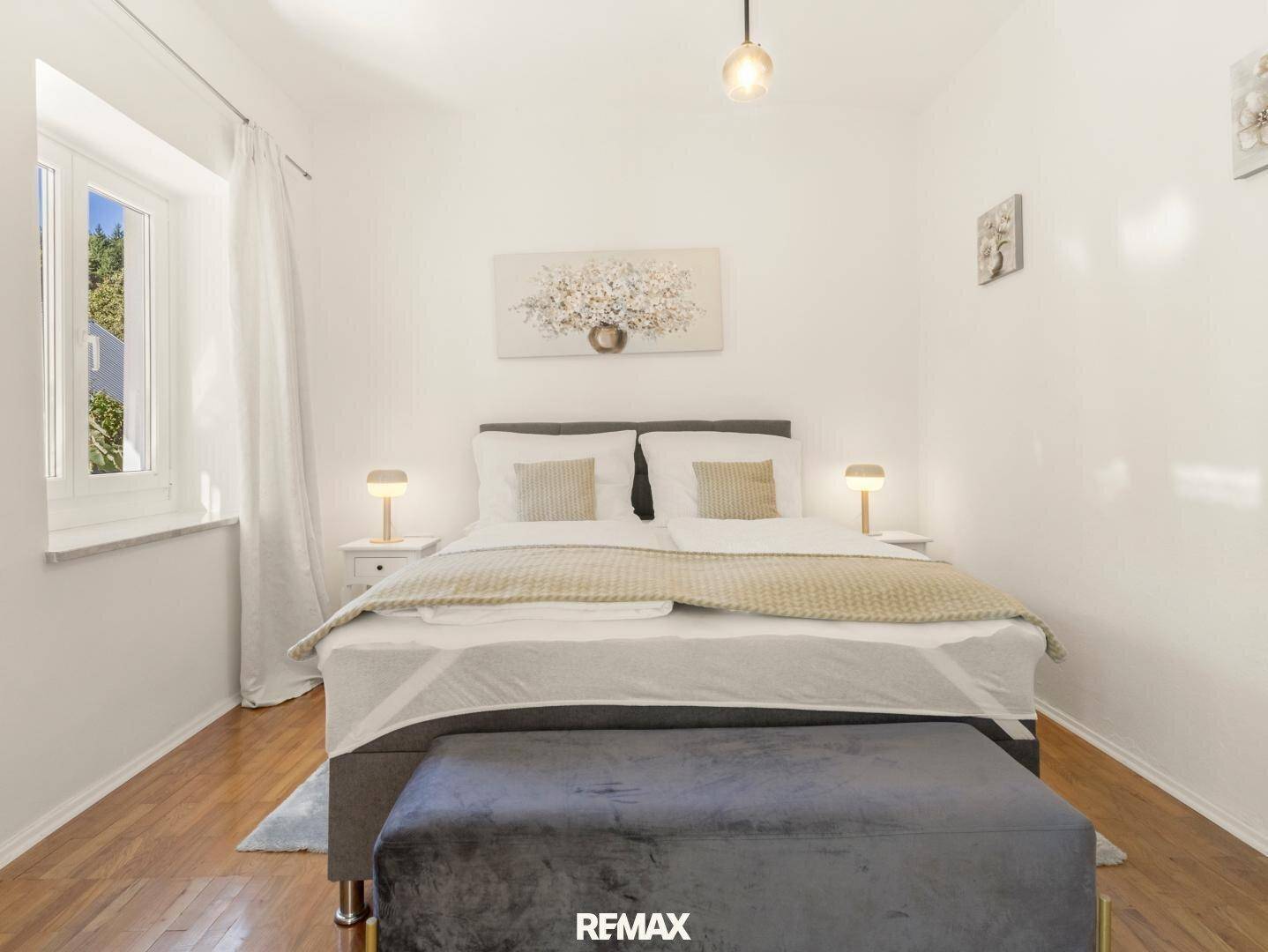 Modernes Schlafzimmer mit Doppelbett, Holzboden und viel Tageslicht durch das Fenster.