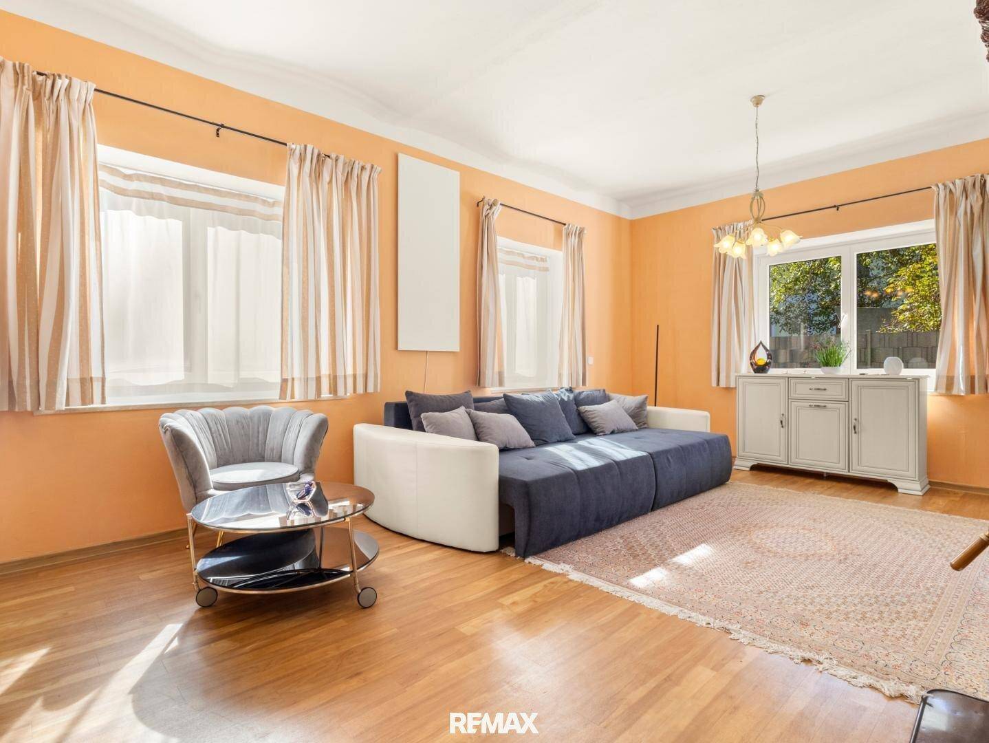 Helles Wohnzimmer mit orangefarbenen Wänden, Sofa und Holzboden, gut beleuchtet.
