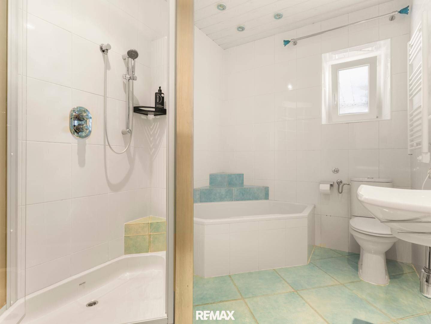 Badezimmer mit Dusche, Eckbadewanne, WC und Fenster, ausgestattet mit hellen Fliesen.