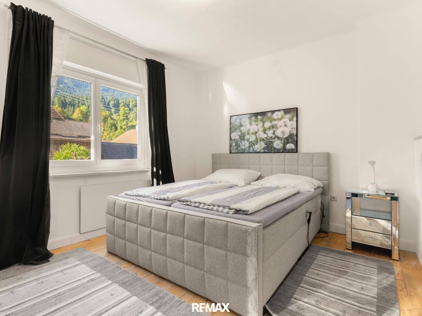 Helles Schlafzimmer mit Doppelbett, Holzboden und Blick ins Grüne durch das Fenster.