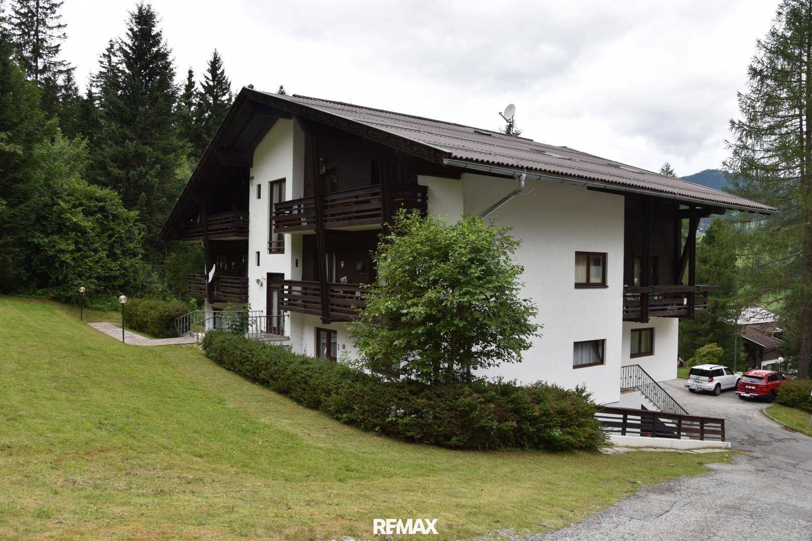 Wohnhaus im alpinen Stil mit Balkonen und gepflegter Grünfläche umgeben von Bäumen.