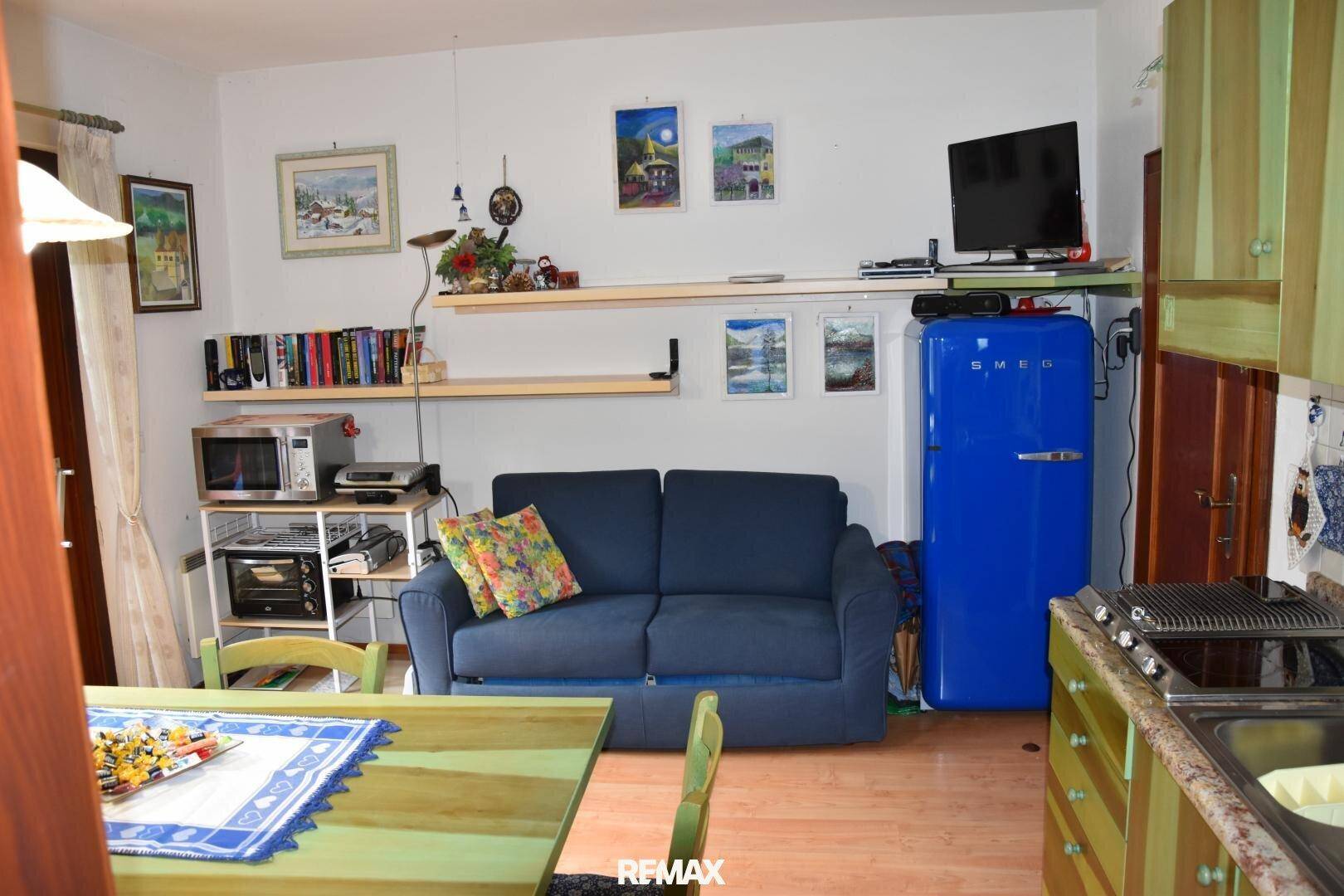 Wohnbereich mit blauem Sofa, Fernseher und einem auffälligen blauen Retro-Kühlschrank.