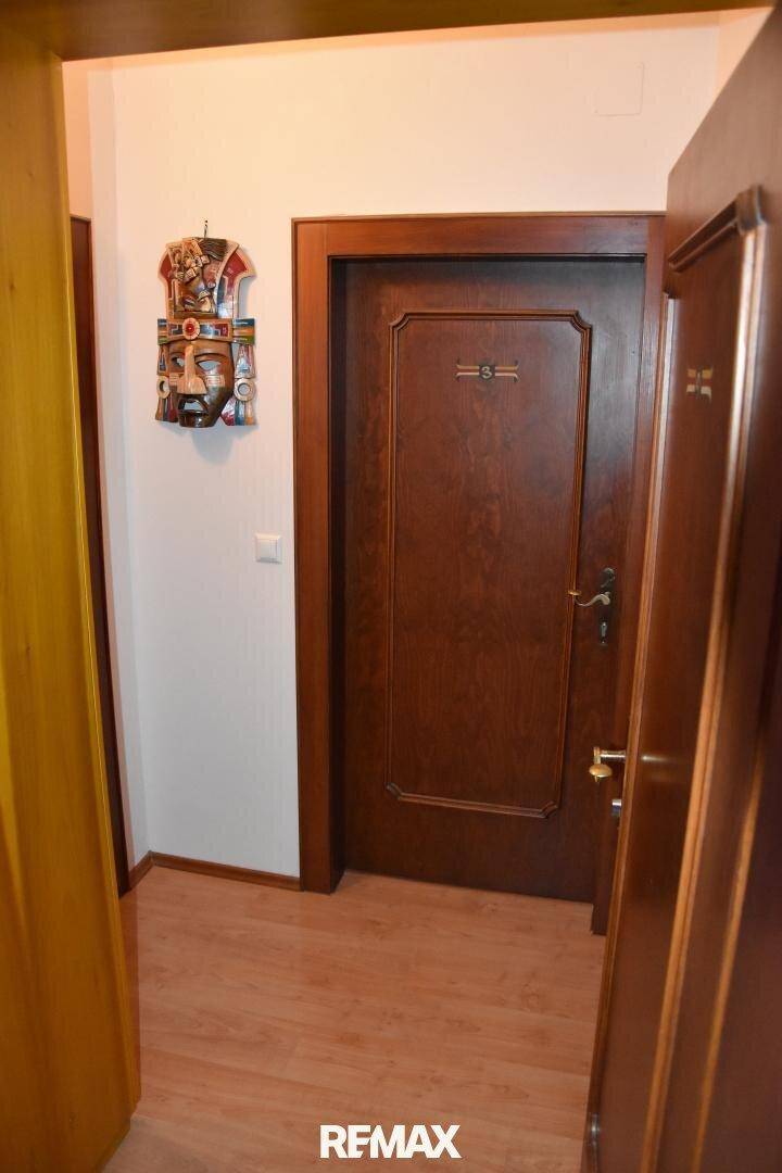 Flur mit dunklen Holztüren und hellem Holzboden, dekoriert mit einer Wandmaske.