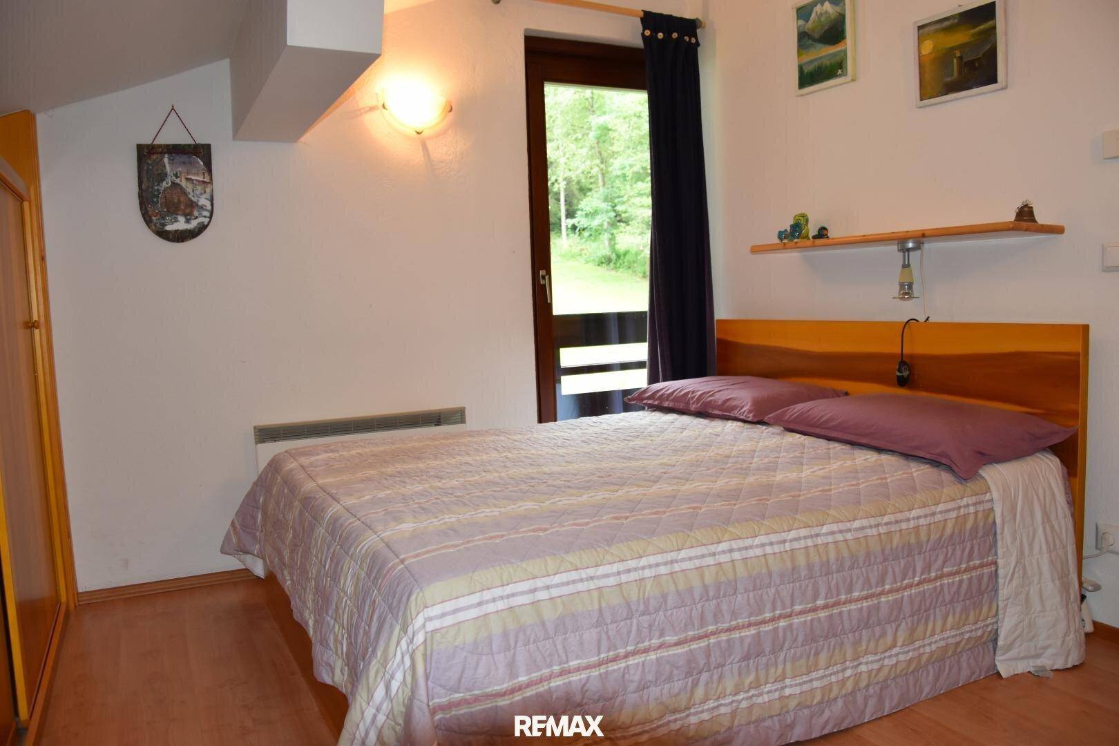 Schlafzimmer mit Doppelbett, Holzmöbeln und Zugang zu einem Balkon mit Waldblick.