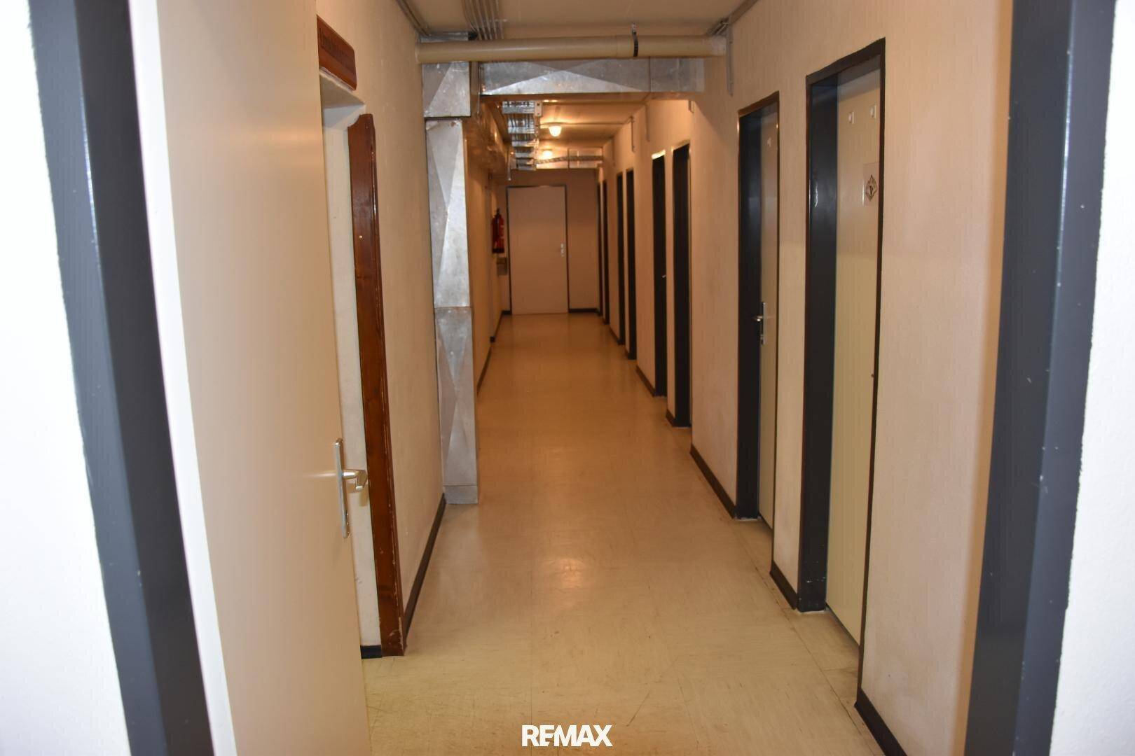 Langer Flur im Untergeschoss mit vielen Türen und sichtbaren Installationen an der Decke.