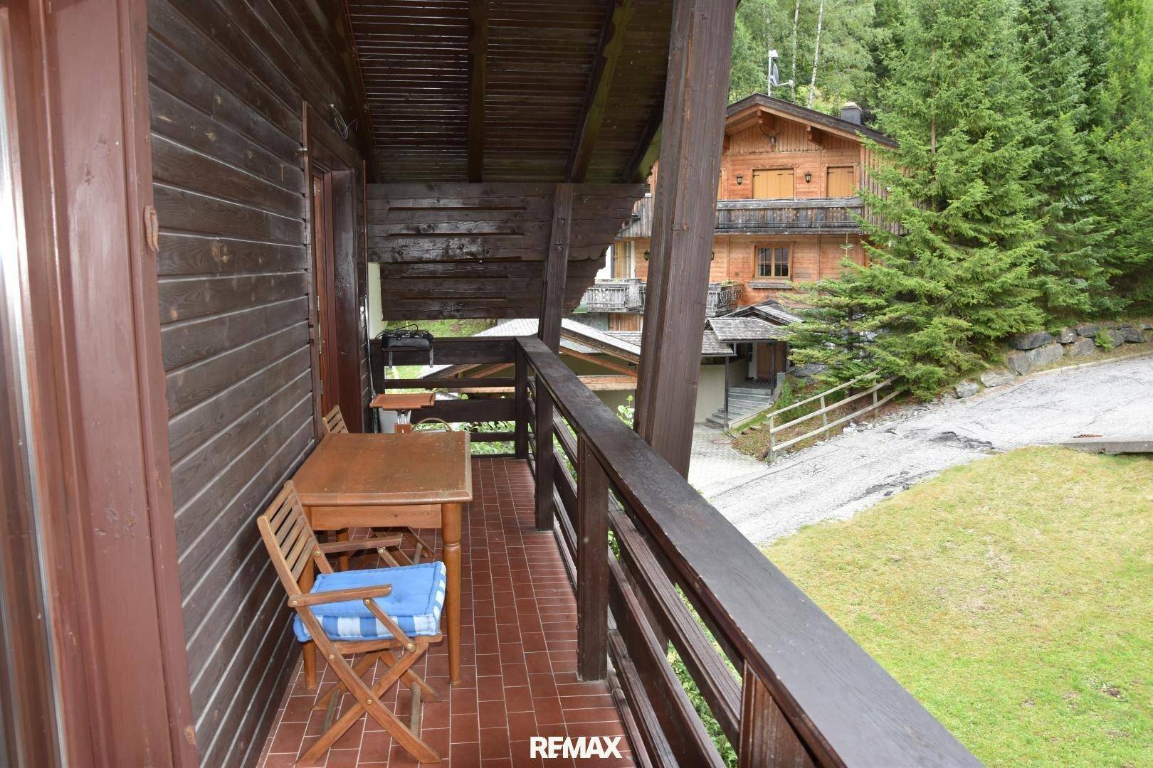 Holzbalkon mit Fliesenboden und Sitzgelegenheit, bietet Blick auf die Umgebung.