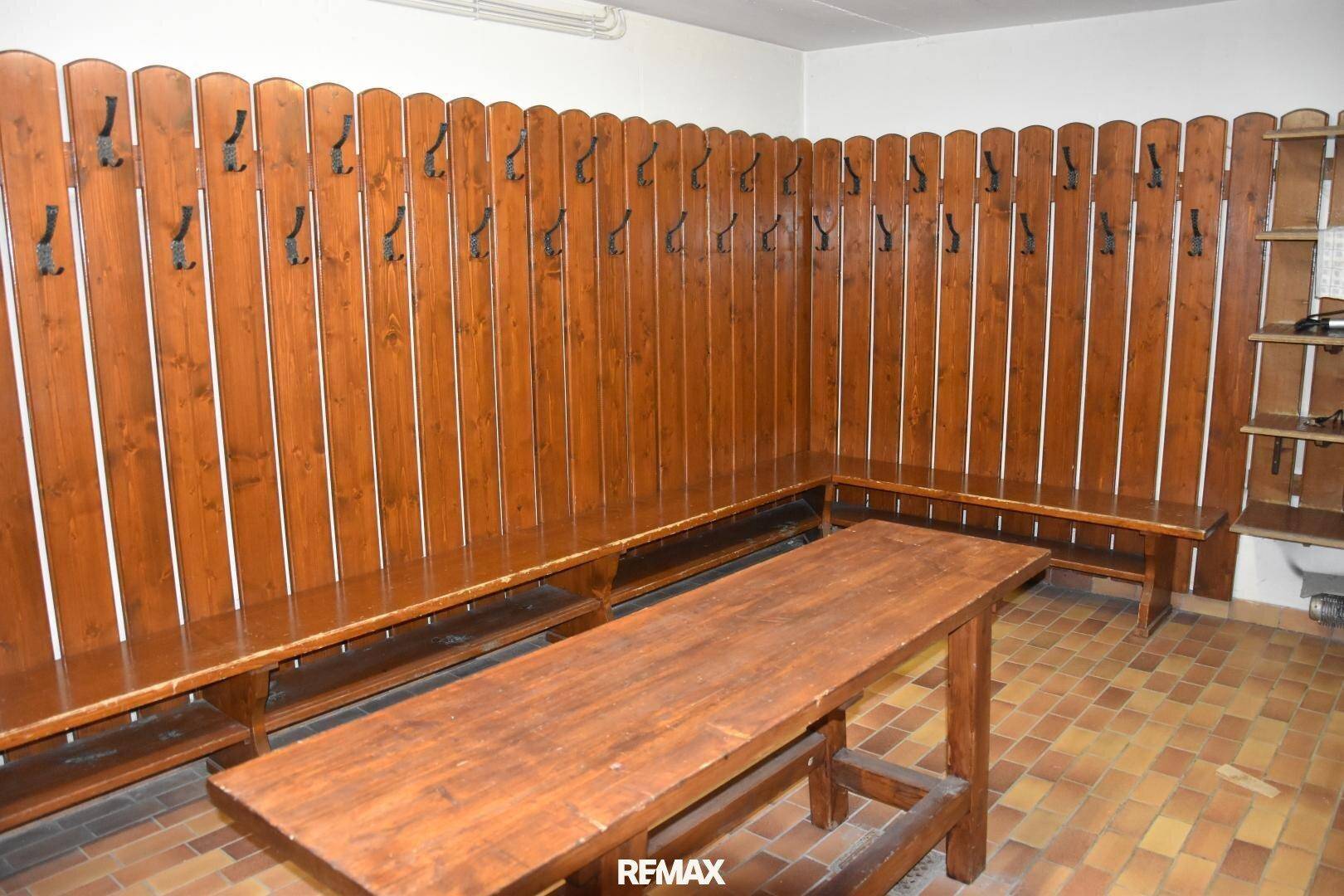 Gemeinschaftlicher Umkleideraum mit Holzbänken und Garderobenhaken, ideal für Skiausrüstung.