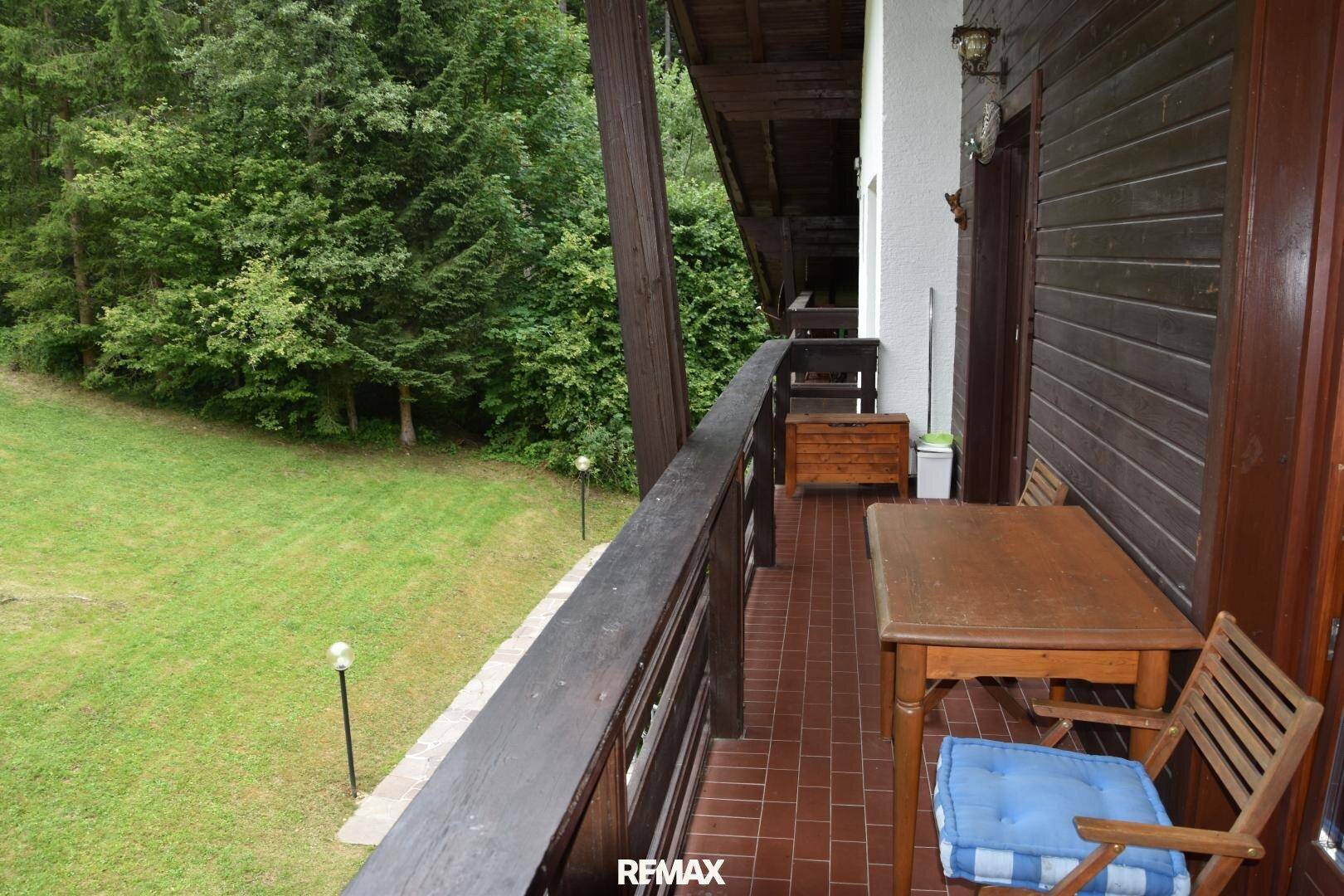 Geräumiger Holzbalkon mit Sitzmöbeln und weitem Blick auf die grüne Landschaft.