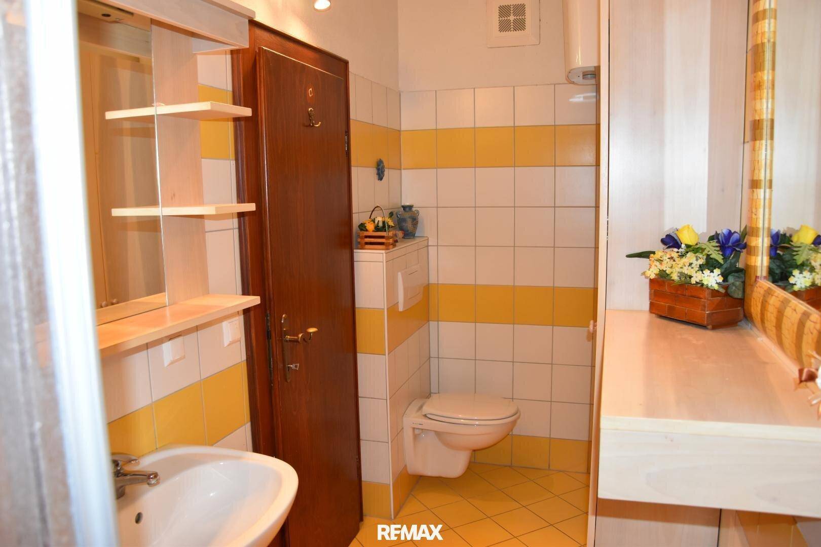 Badezimmer mit gelb-weißen Fliesen, Toilette, Waschbecken und Spiegelschrank.