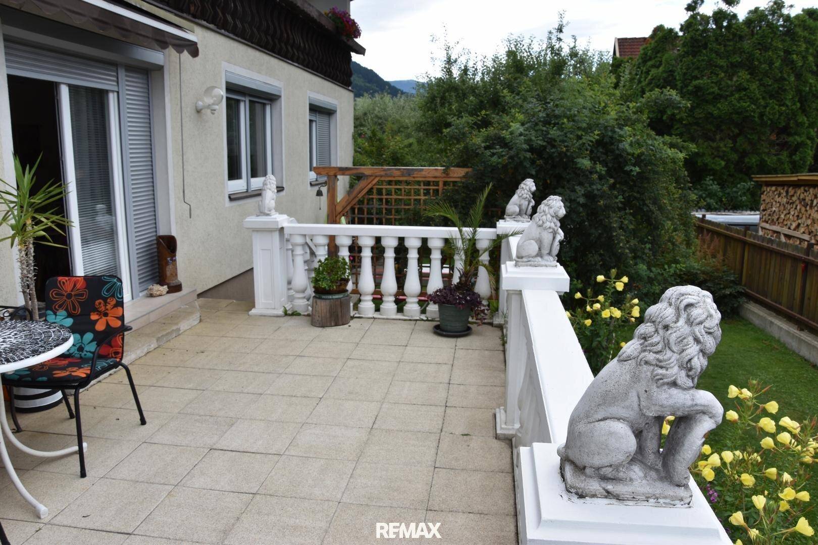 Geräumige geflieste Terrasse mit Balustrade, Löwenstatuen und Blick auf den grünen Gartenbereich.
