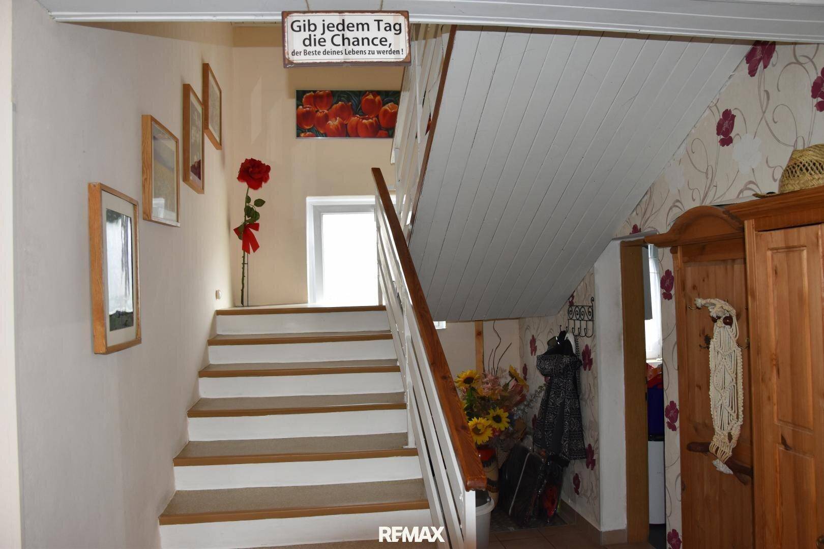 Holztreppe mit weiß gestrichenen Stufen und Geländer, führt zu einem oberen Stockwerk mit Fenster.