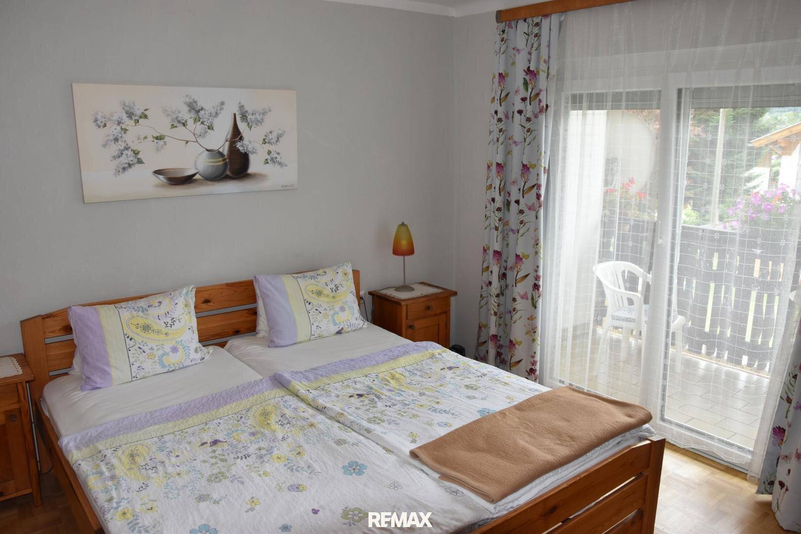 Schlafzimmer mit zwei Einzelbetten, Holzbettrahmen und Zugang zu einem Balkon mit Blick ins Grüne.