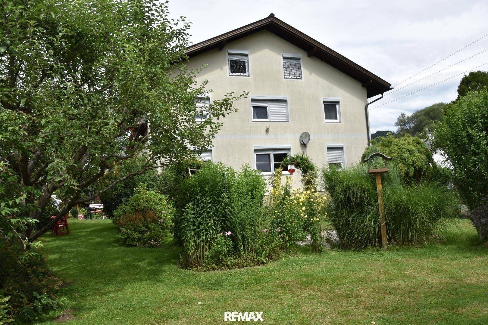 Großer, gepflegter Garten mit Rasen, üppiger Bepflanzung und der Rückseite des Wohnhauses.