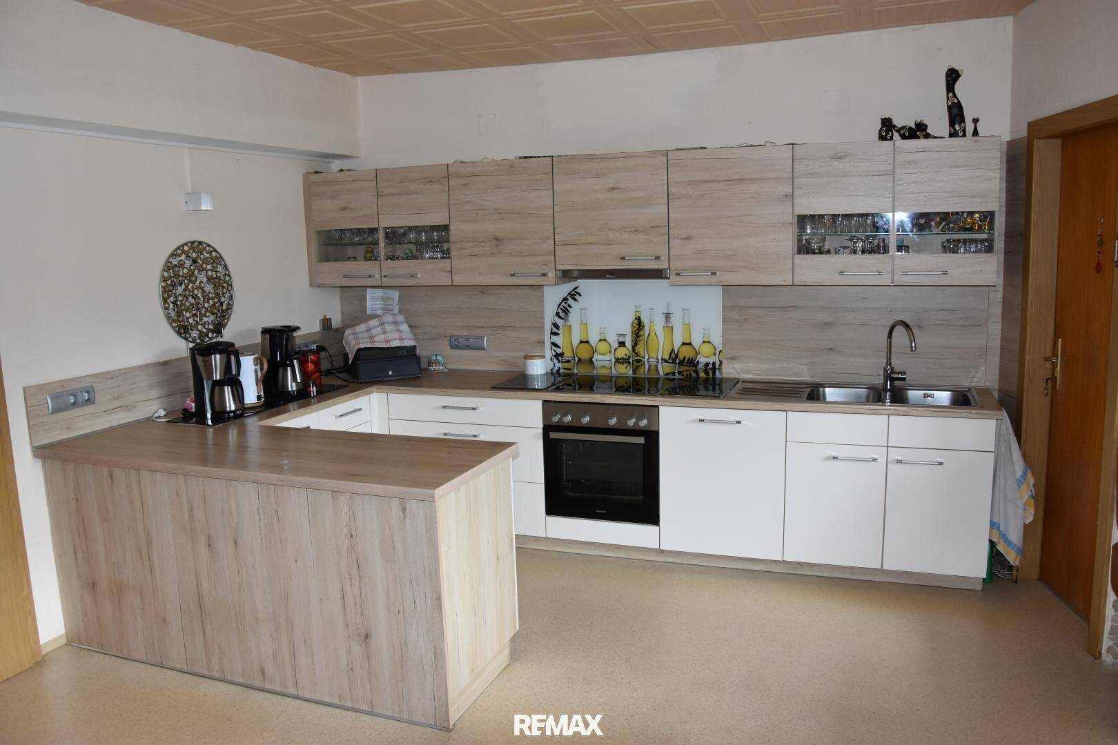 Moderne Küche mit hellen Holz- und weißen Fronten, integrierten Geräten und einer Frühstückstheke.