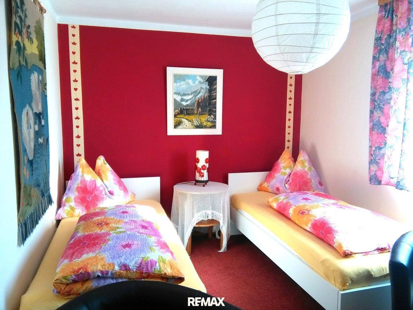Schlafzimmer mit roten Akzentwänden, zwei Einzelbetten und einer Papierlampe, mit Teppichboden.