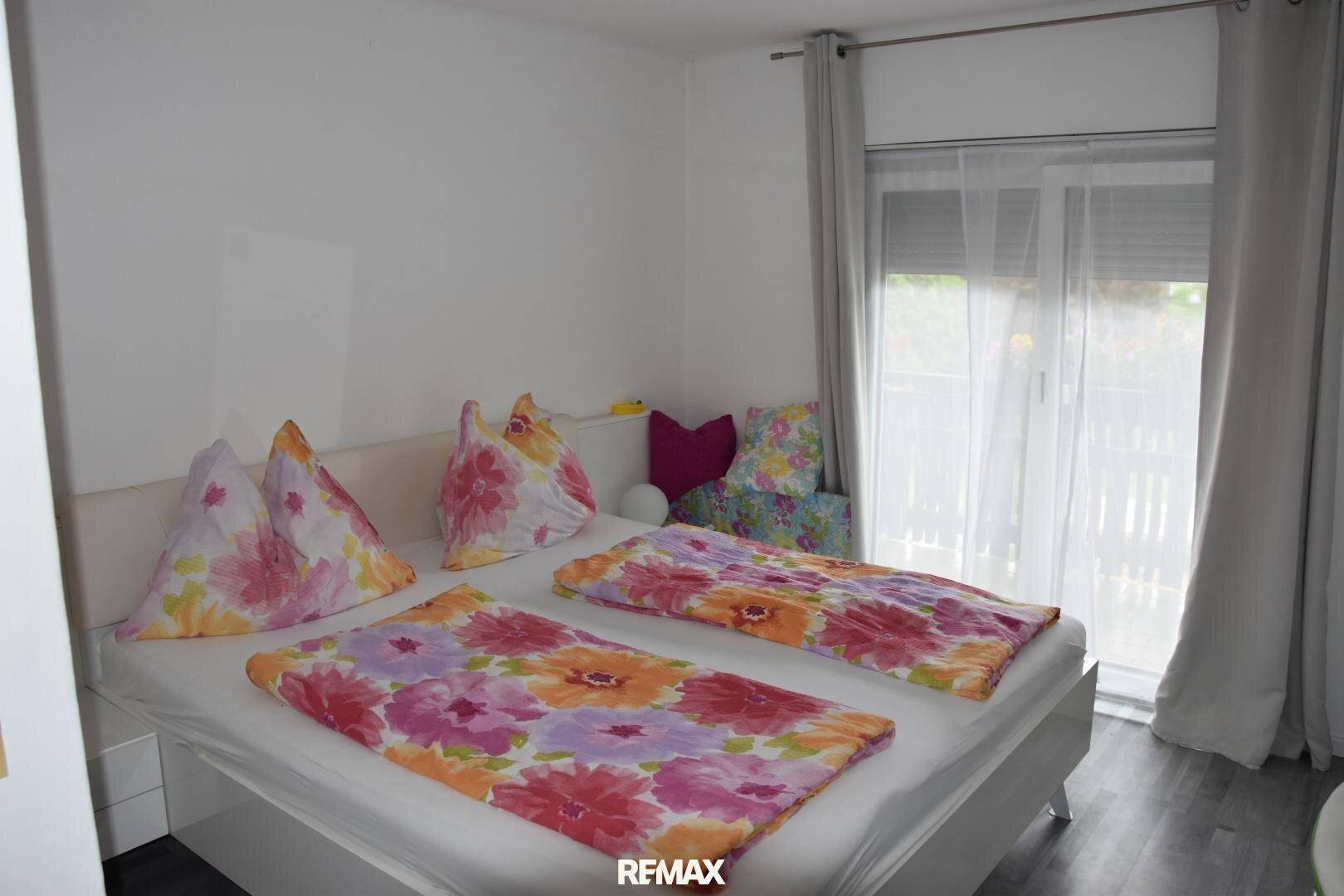 Schlafzimmer mit Doppelbett und farbenfroher Bettwäsche, Zugang zu einem Balkon mit Jalousien.