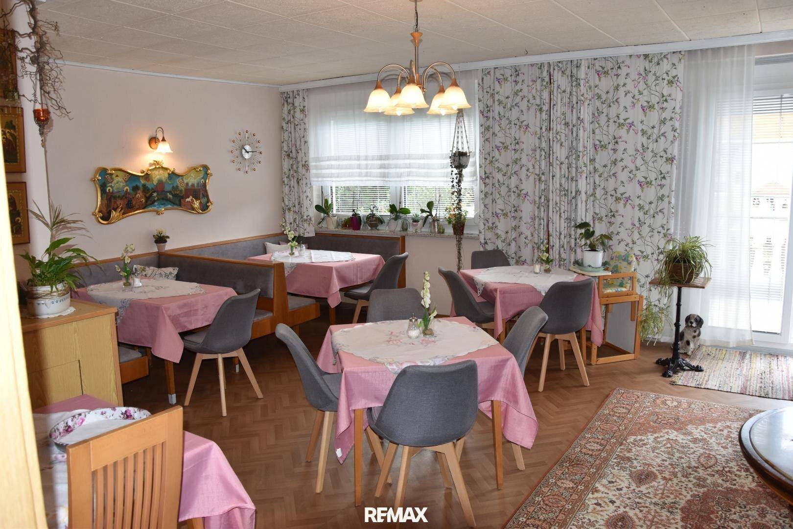 Geräumiger Speisesaal mit mehreren Tischen, Stühlen, einer Eckbank und floralen Vorhängen.