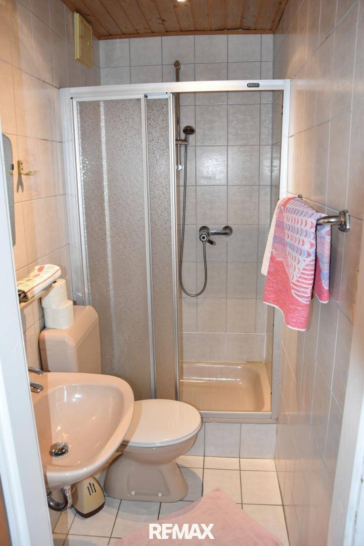 Kleines Badezimmer mit Duschkabine, WC und Waschbecken, ausgestattet mit hellen Fliesen und Holzdecke.