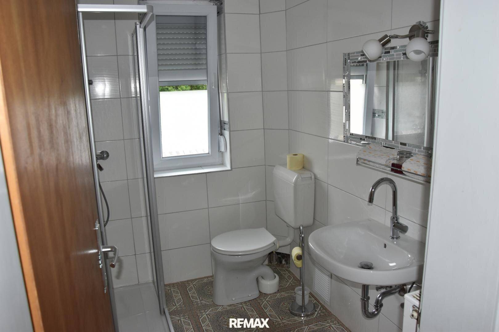 Helles Badezimmer mit Duschkabine, WC, modernem Waschbecken und Fenster für natürliche Belüftung.