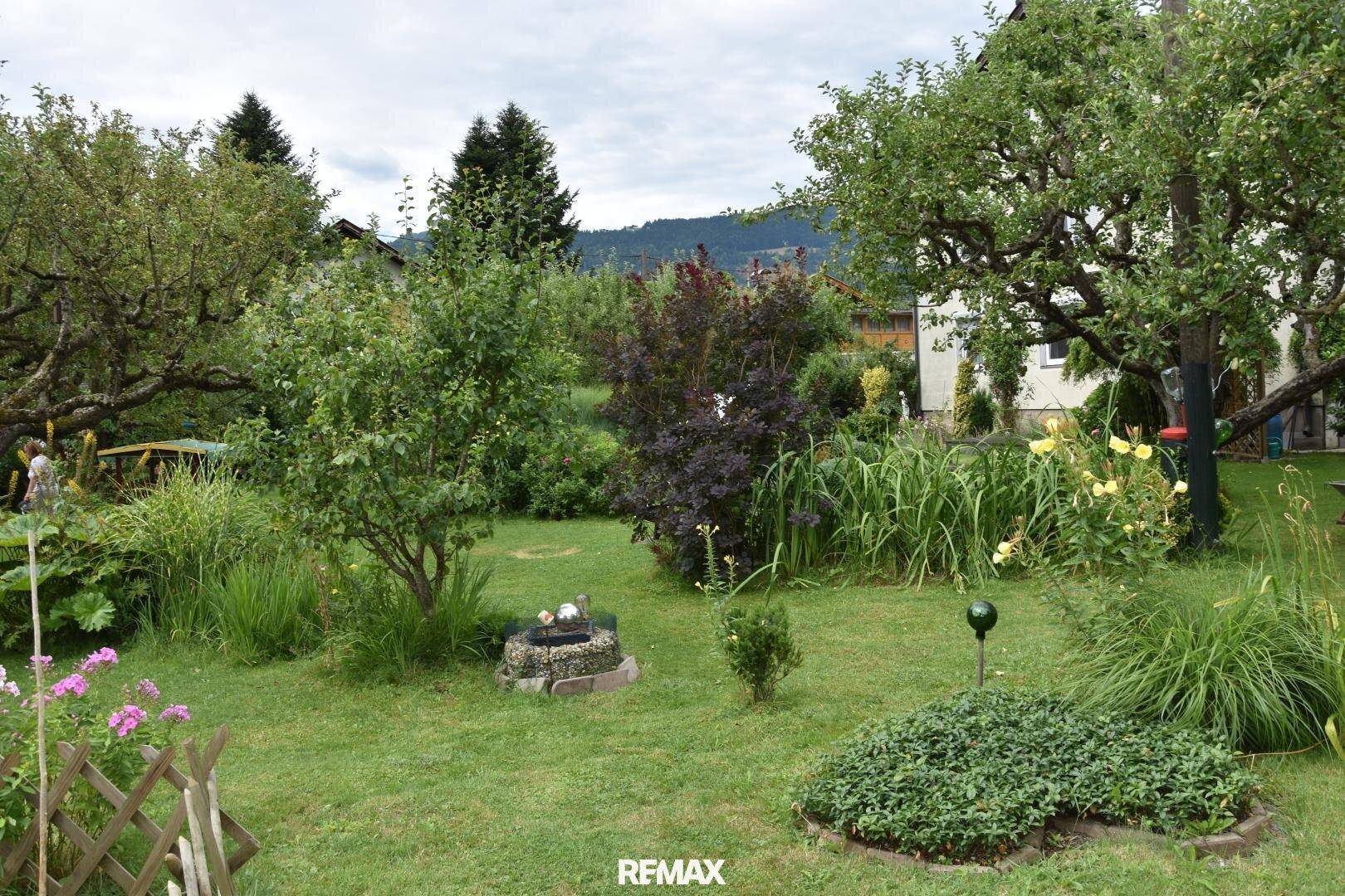 Weitläufiger Garten mit verschiedenen Pflanzen, Rasenflächen und einem kleinen dekorativen Brunnen.