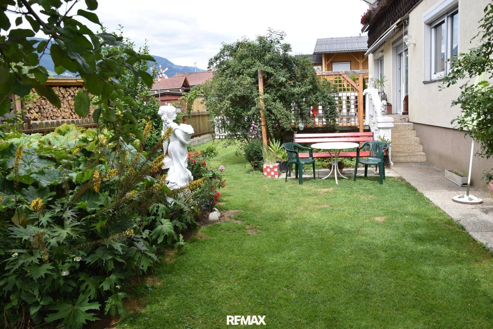 Gepflegter Gartenbereich mit Rasen, Blumenbeeten und einer Sitzgruppe neben dem Haus.