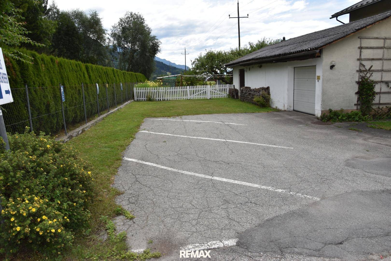 Außenparkplätze und eine Garage neben dem Haus, umgeben von einer hohen Hecke.