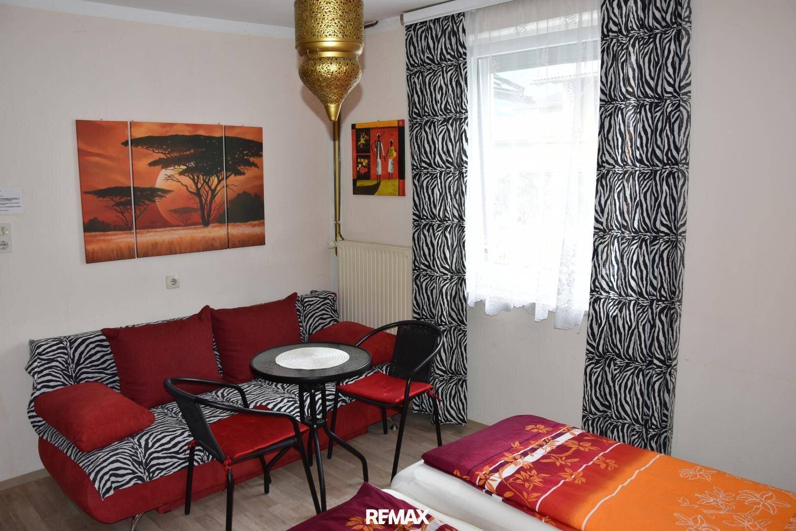 Schlafzimmer mit Sofa, kleinem Tisch und auffälligen Zebra-Vorhängen.