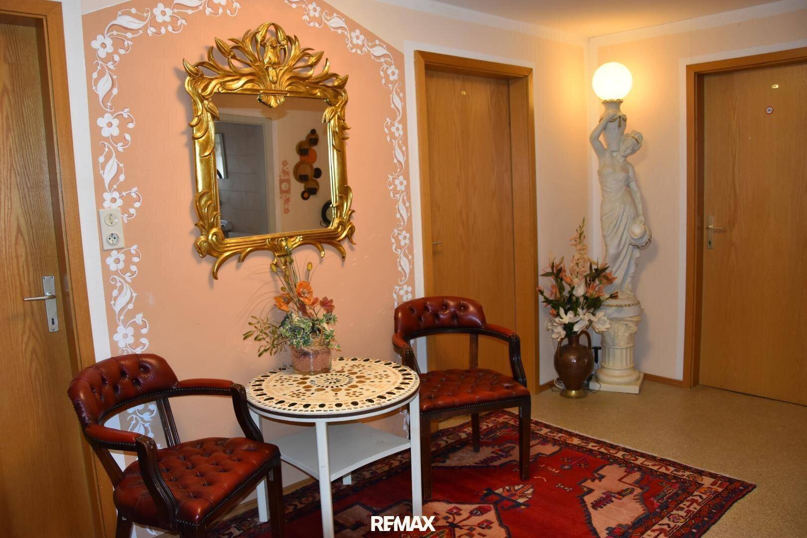 Eingangsbereich mit opulentem Spiegel, kleiner Sitzecke und einer dekorativen Statue mit Lampe.