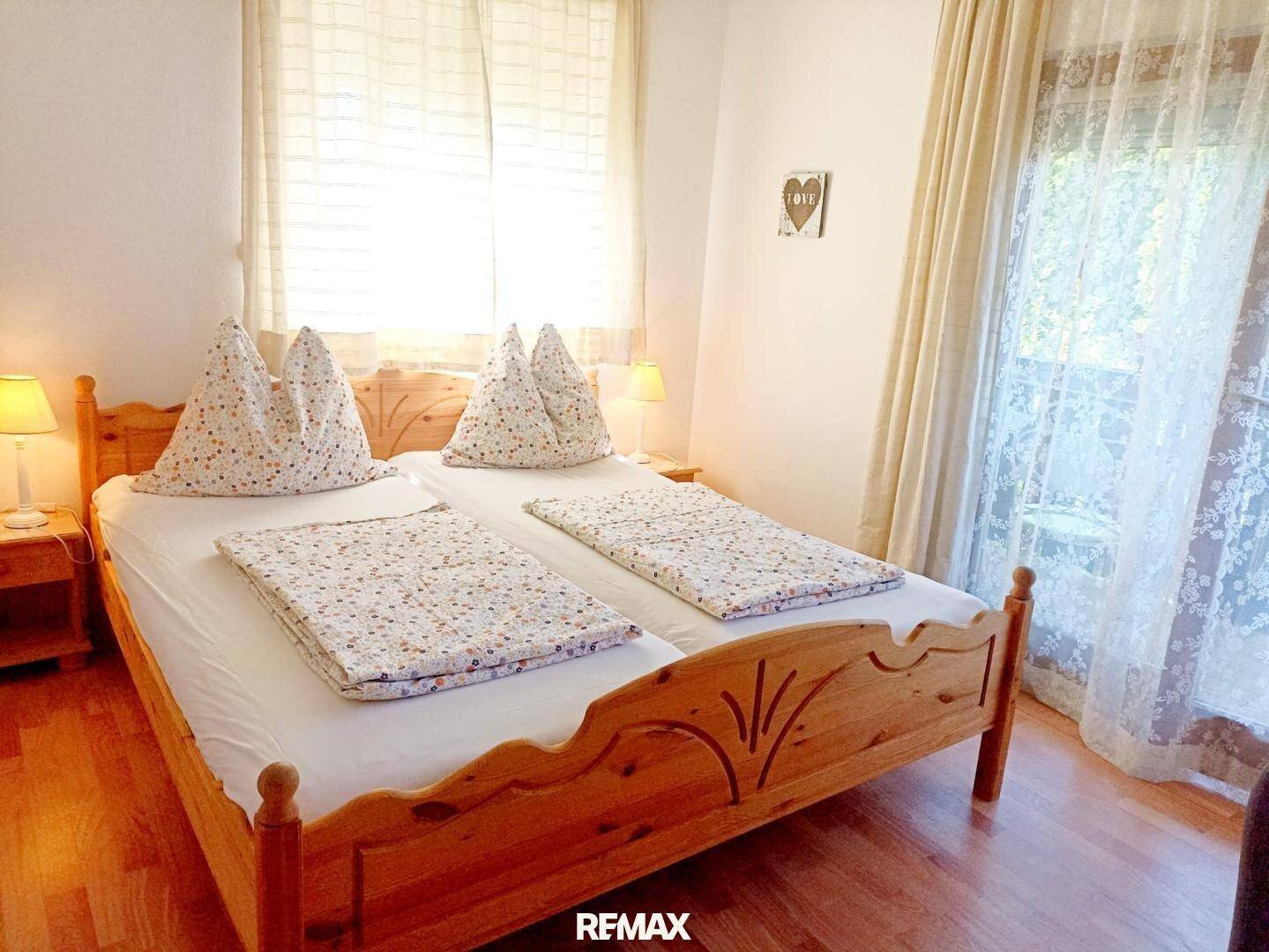 Gemütliches Schlafzimmer mit zwei Einzelbetten aus Holz, Holzboden und Balkonzugang.