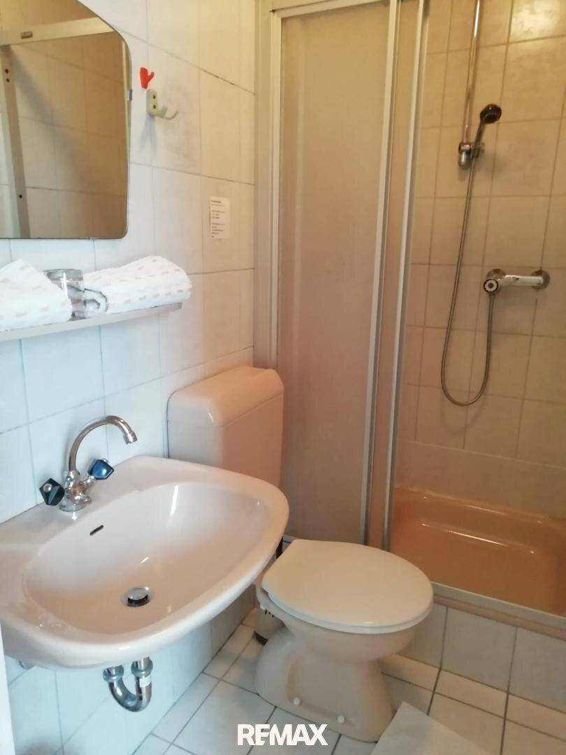 Kleines Badezimmer mit Duschkabine, WC und Waschbecken, ausgestattet mit hellen Fliesen.