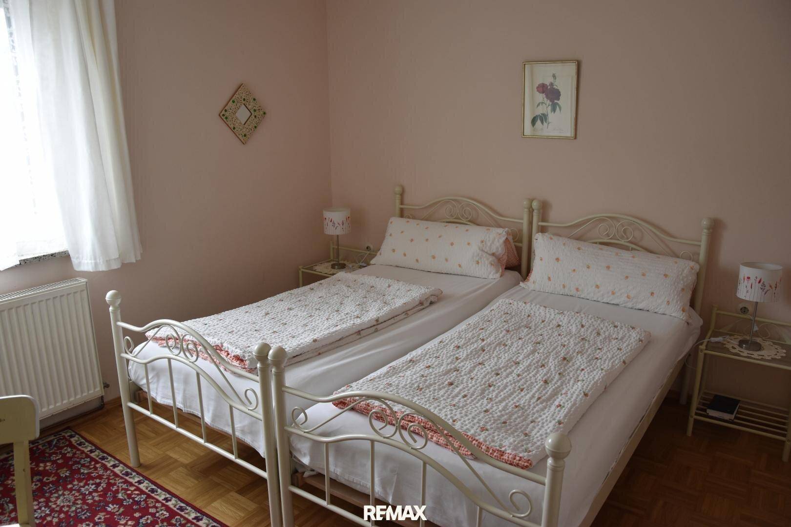 Helles Schlafzimmer mit zwei Einzelbetten in verschnörkelten Metallrahmen und rosa Wänden.