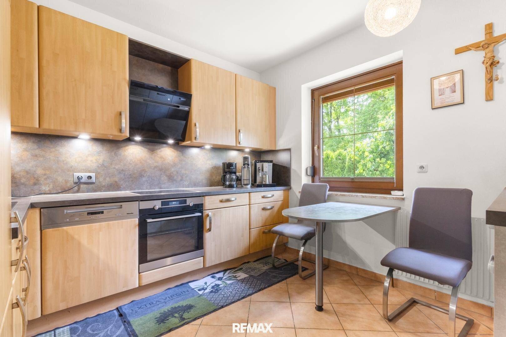 Funktionale Küche mit Holzeinbauschränken, Essbereich und Fenster mit Blick ins Grüne.