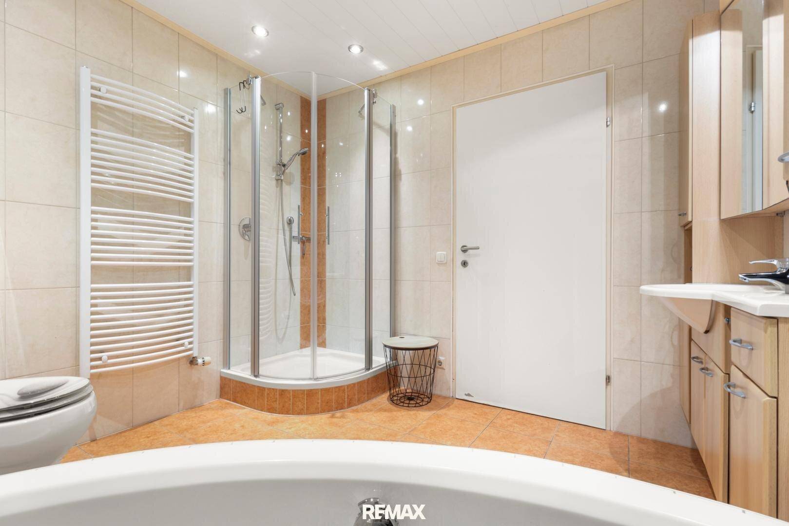 Helles Badezimmer mit Badewanne, Duschkabine, Fliesenboden und Holzmöbeln.
