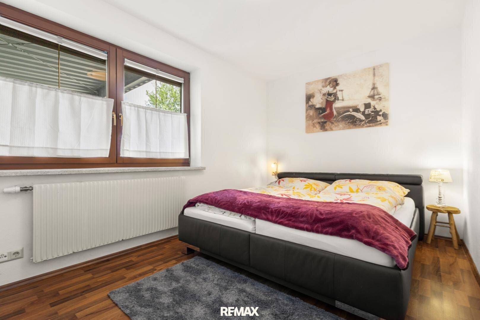 Gemütliches Schlafzimmer mit Doppelbett, Holzboden und Fenster mit Blick ins Grüne.