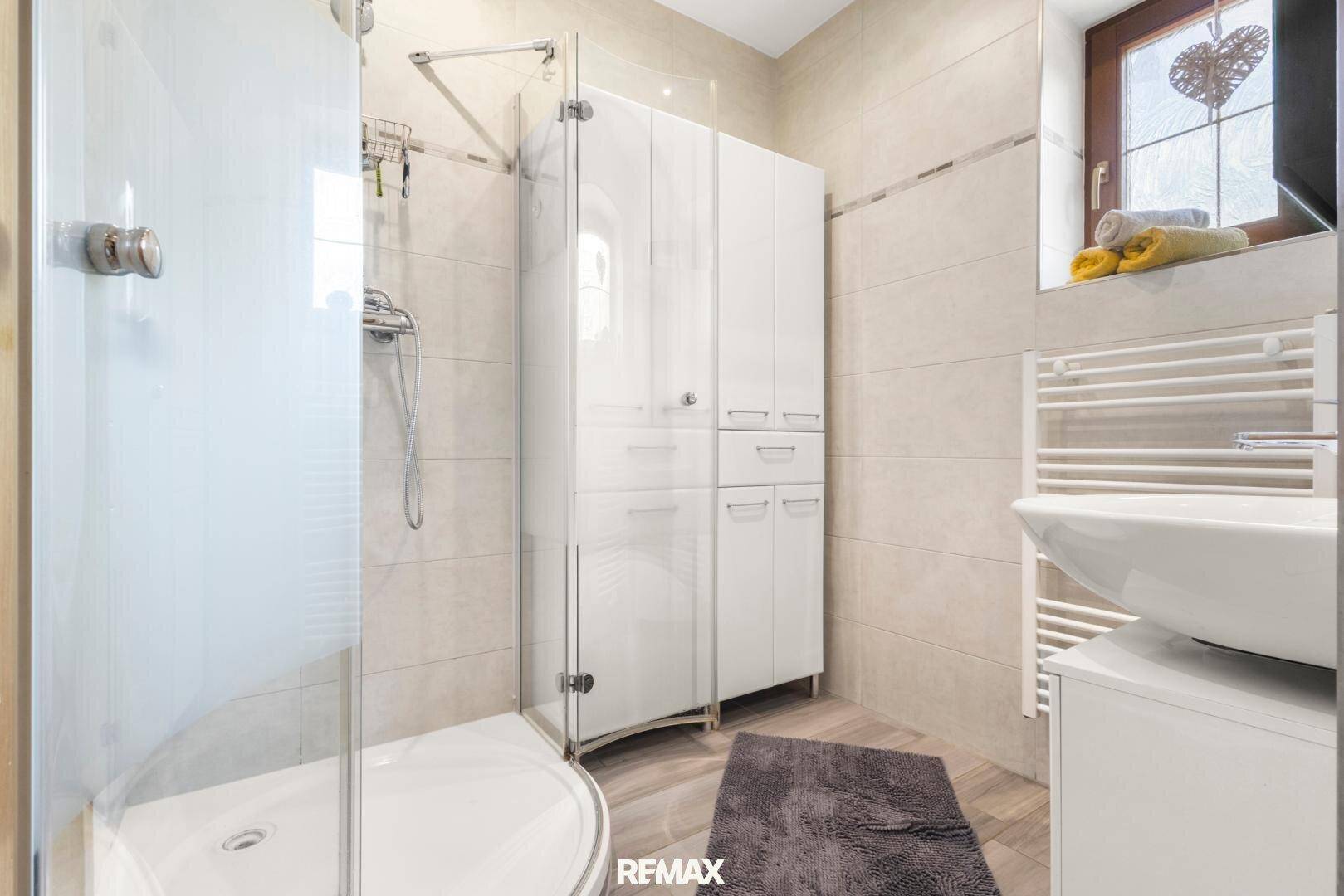 Modernes Badezimmer mit Duschkabine, weißen Schränken und beheiztem Handtuchhalter.