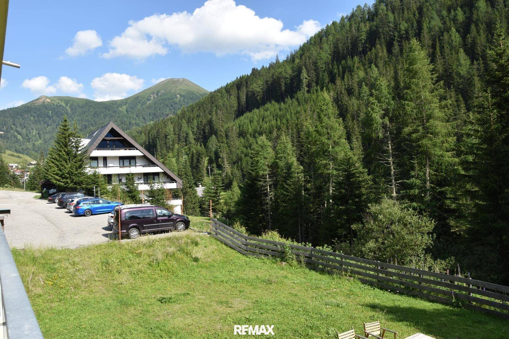 Gebäudekomplex in den Bergen mit Parkplätzen, umgeben von dichtem Wald und einer weiten Berglandschaft.
