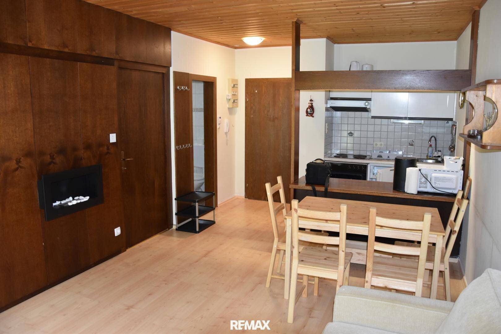 Wohn-Essbereich mit integrierter Küchenzeile, Holztisch und Einbauschränken unter einer Holzdecke.