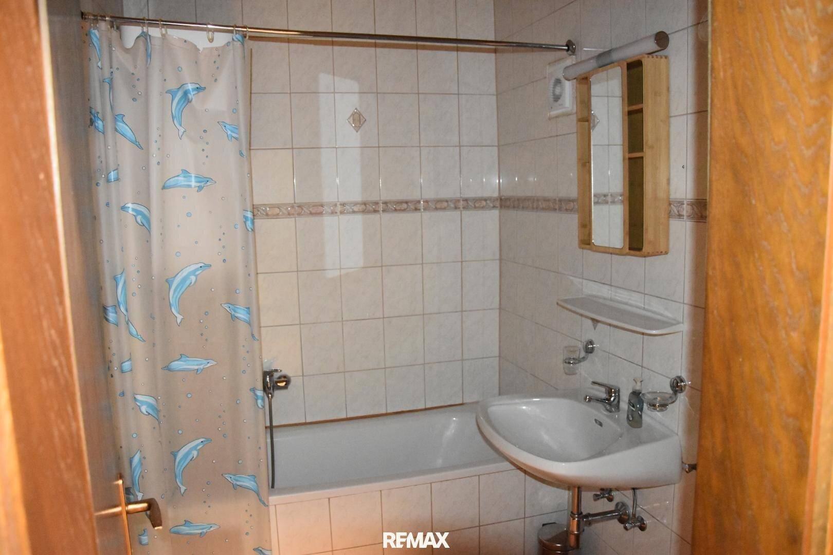 Badezimmer mit Badewanne, Waschbecken und Fliesen in hellem Beige, ausgestattet mit Duschvorhang.