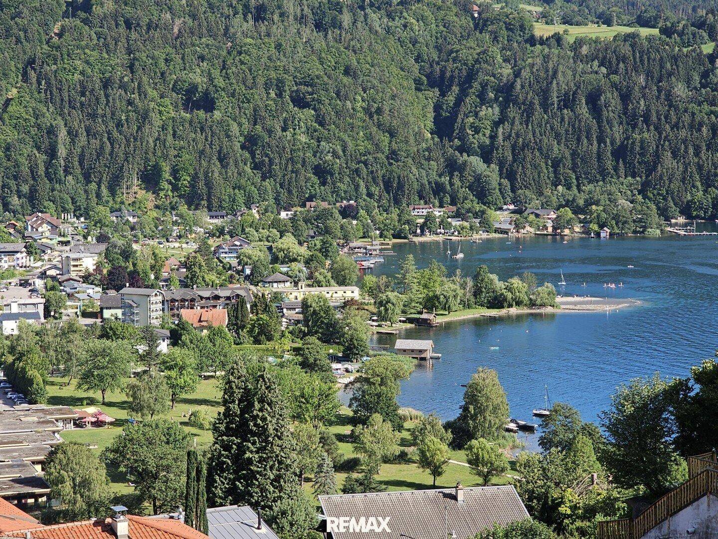 Blick auf eine malerische Stadt am Seeufer, umgeben von dichten Wäldern und Bergen.