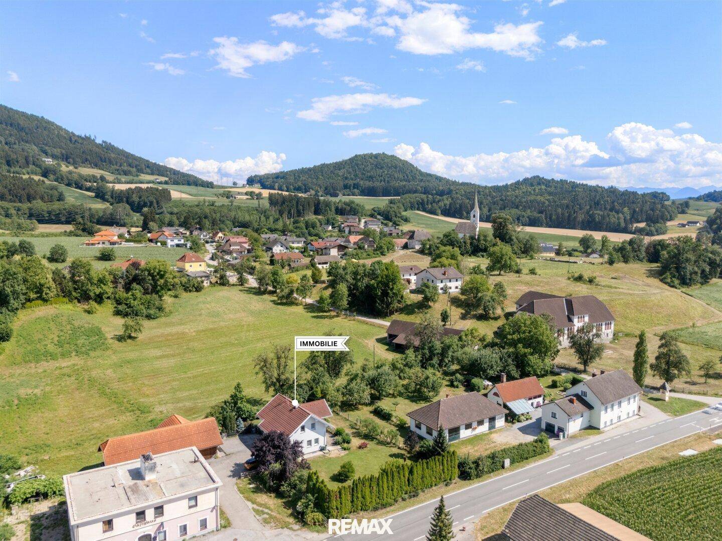Weitläufige Luftaufnahme des Anwesens in einer ländlichen Umgebung mit Dorf und Bergen im Hintergrund.