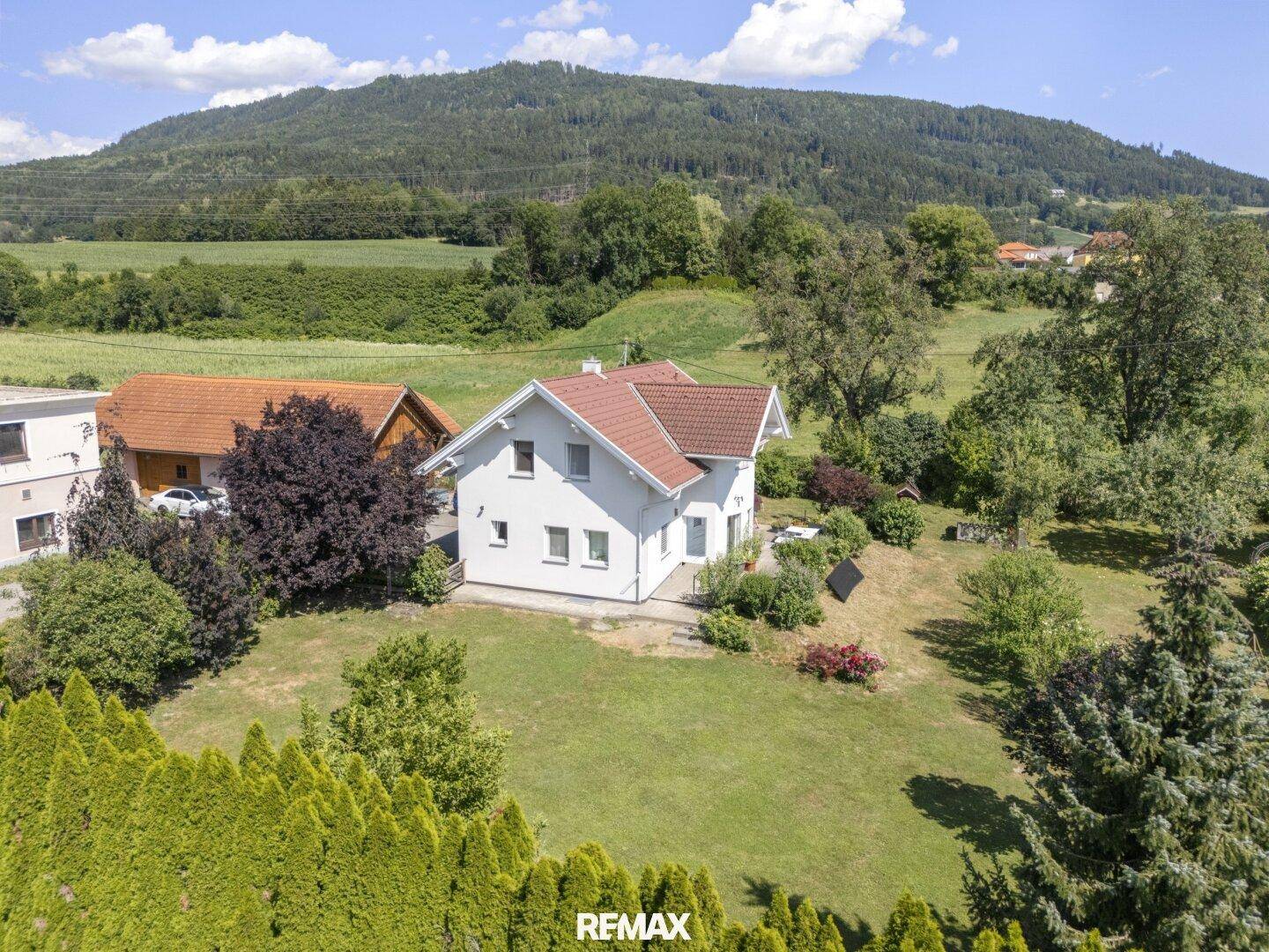 Luftaufnahme eines Einfamilienhauses mit großem Garten und Blick auf die umliegende Hügellandschaft.
