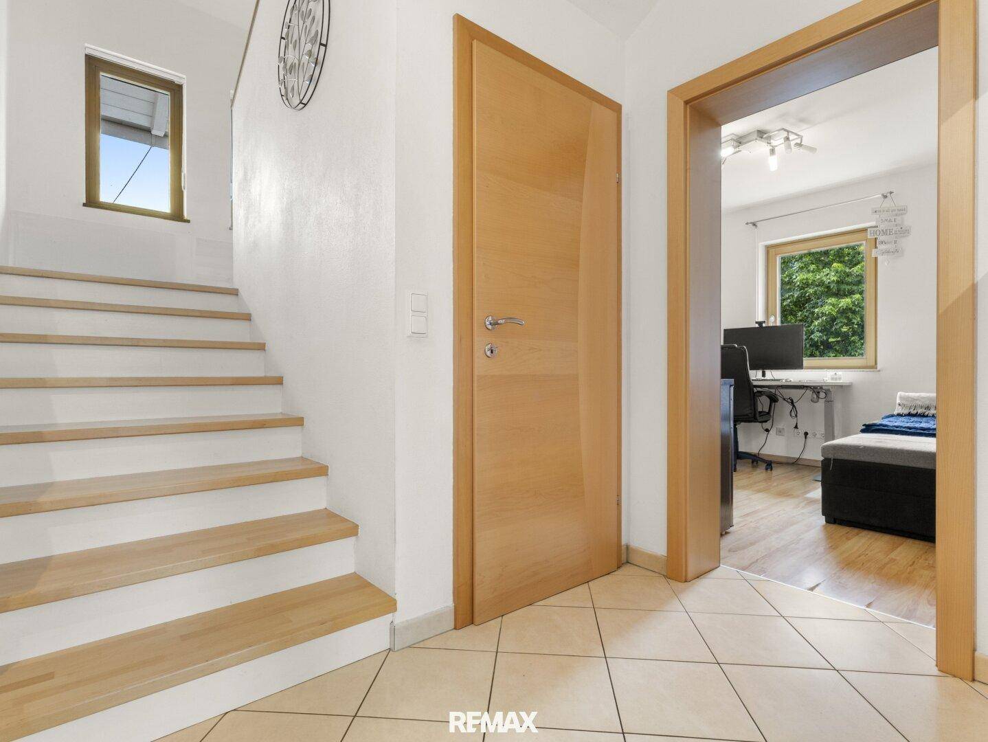 Heller Flur mit Holztreppe und Zugang zu weiteren Räumen, gefliestem Boden.